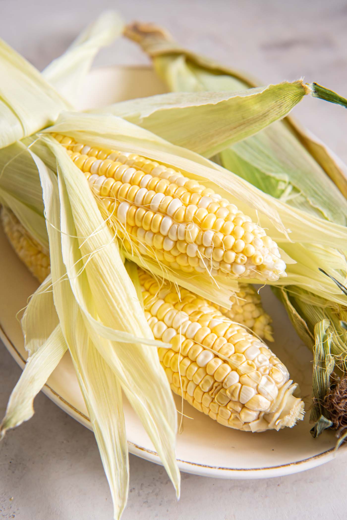 Learn how to make the best air fryer corn on the cob! This easy recipe makes delicious sweet corn that's juicy and tender inside. Recipe post includes how to pick the best fresh corn. Partially shucked corn cobs on a plate.